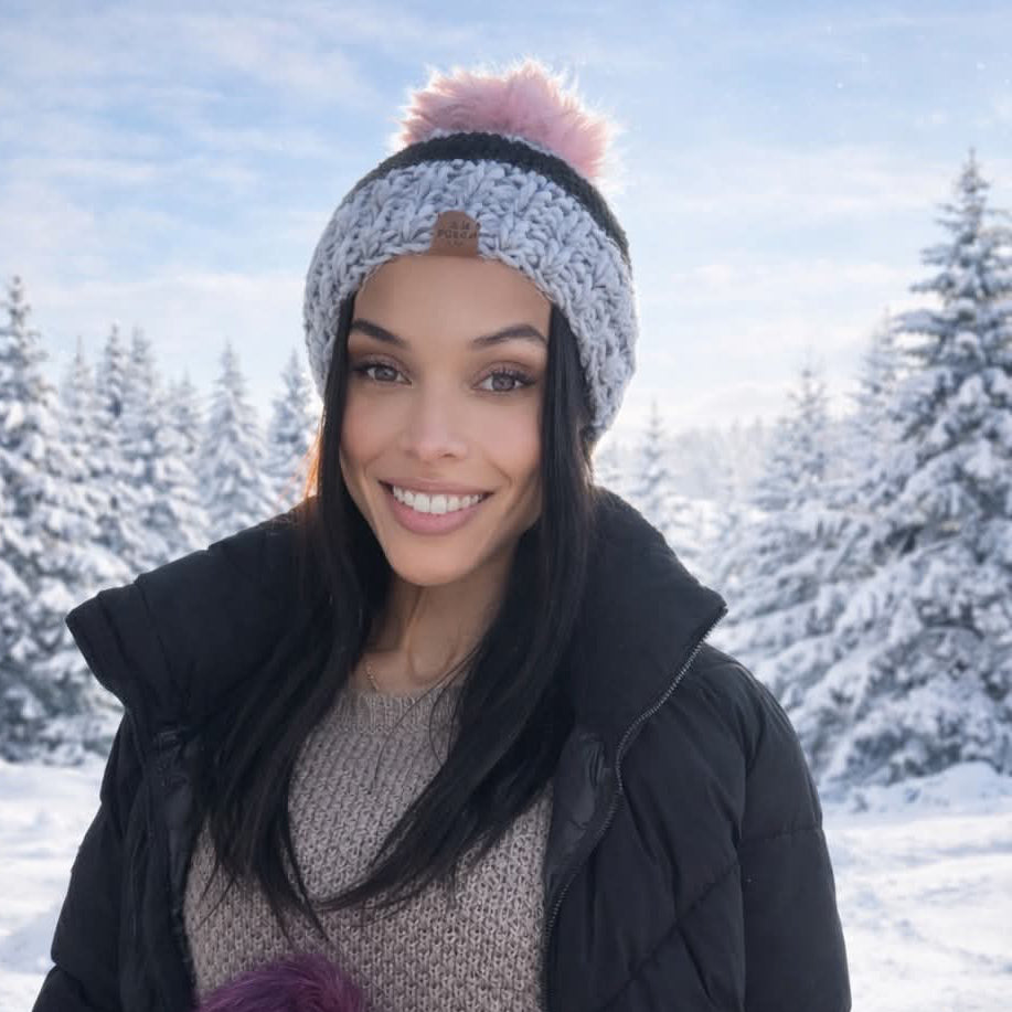 Woman in winter clothing standing in a snowy landscape with trees wearing behappe knit pom hat