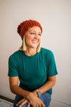 Woman wearing a green shirt and orange slouchy beanie smiling against a plain background