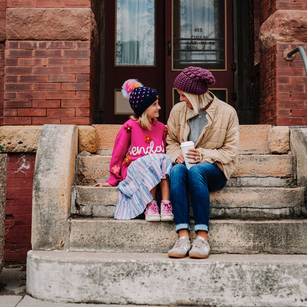 Brooke Happe and daughter sitting on a set of stone steps in front of a brick building wearing behappe beanies