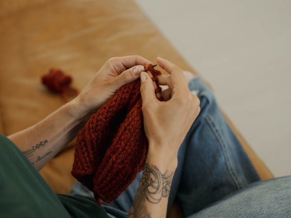 Brooke Happe knitting with red yarn on a wooden surface