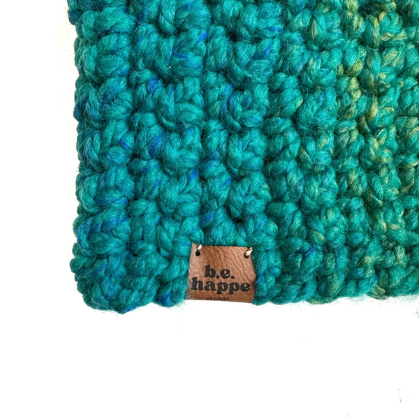 Close-up of a teal crochet slouch hay fabric with a brand tag on a white background