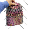 A multicolored crochet slouch hat being held by a hand, featuring a puff stitch design in purple and gray tones.