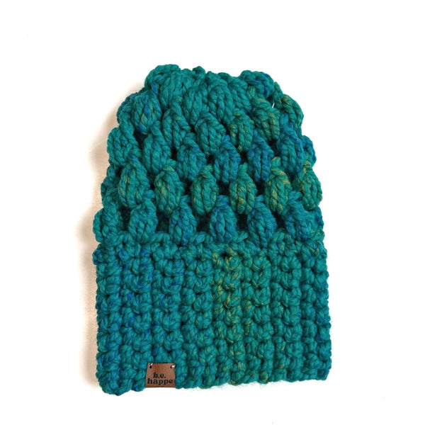 Teal crochet slouch hat with brand label on a white background