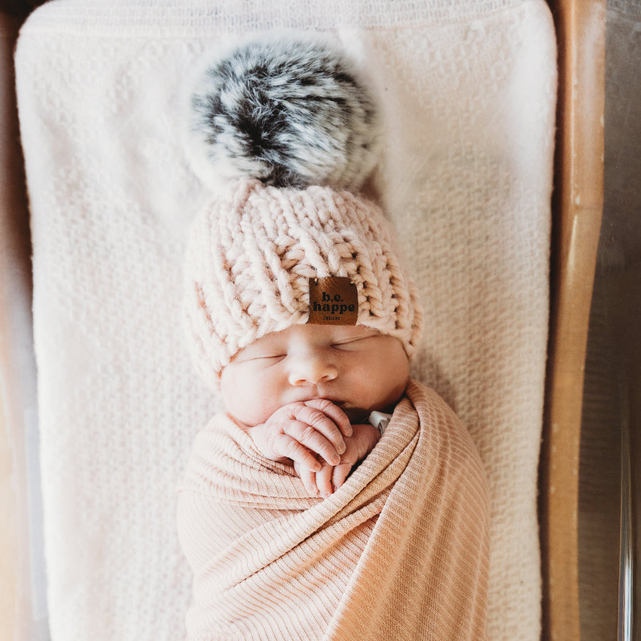 Newborn baby wrapped in a pink blanket with a matching pink behappe hat on a wooden surface
