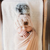 Newborn baby wrapped in a pink blanket with a matching pink behappe hat on a wooden surface