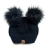 Black knit beanie with two large black pom-poms on a white background