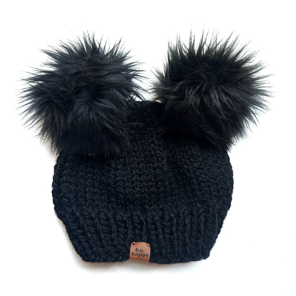 Black knit beanie with two large black pom-poms on a white background
