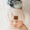 Newborn baby wrapped in a pink blanket with a pink behappe knit hat, lying on a white surface.