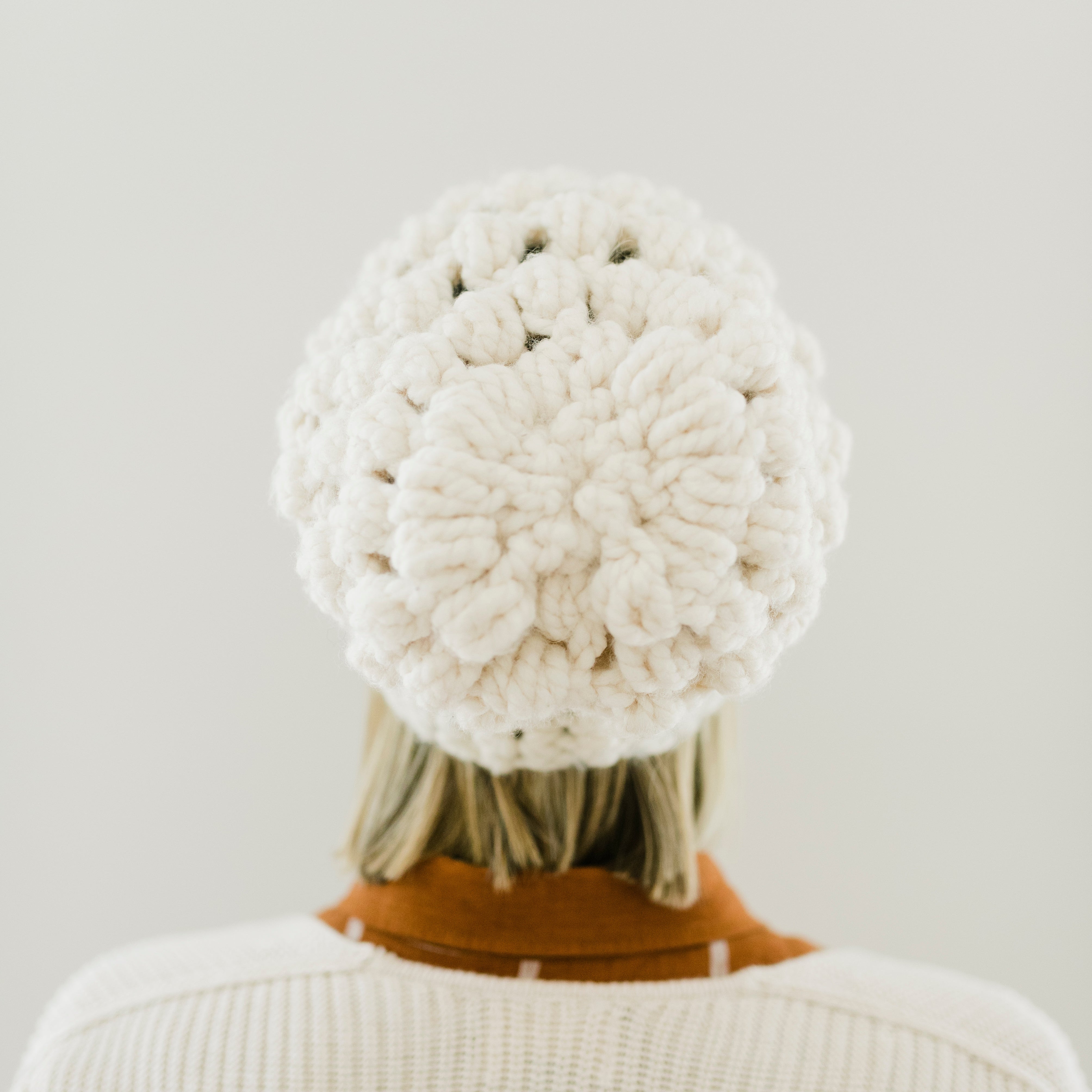 Person wearing a white knit beanie and sweater against a plain background