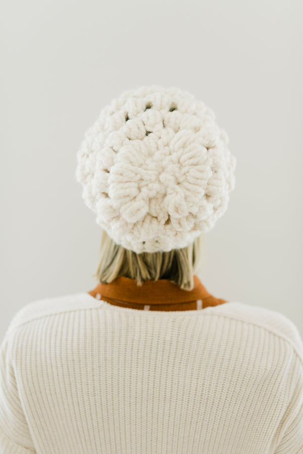 Person wearing a white knit beanie and sweater against a plain background
