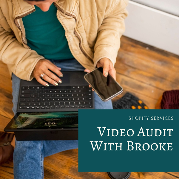 A person sitting on a wooden floor uses a laptop and phone while wearing a tan jacket and blue jeans. A large teal text box in the lower right reads 'SHOPIFY SERVICES VIDEO AUDIT WITH BROOKE'.