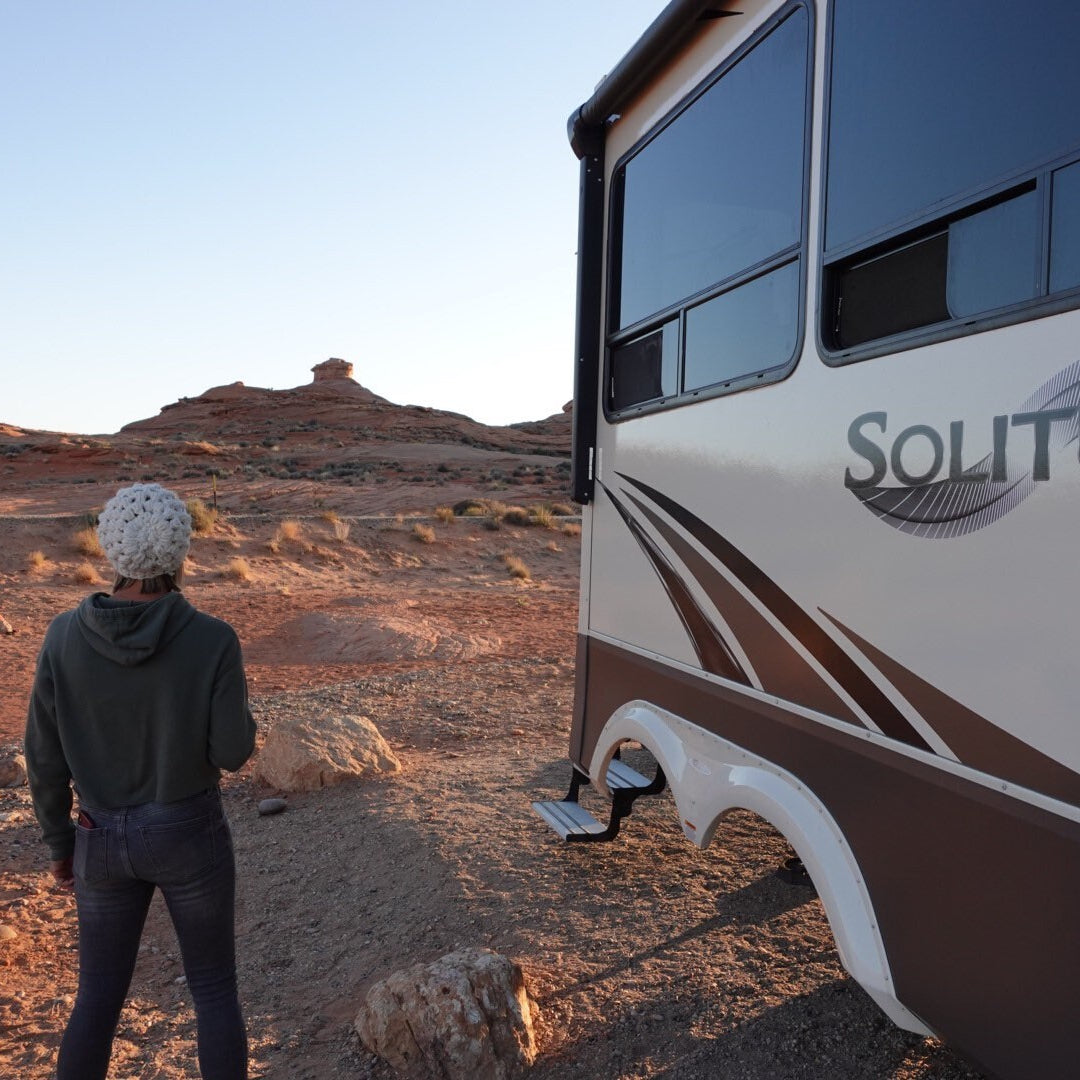 Person standing wearing b.e.happe slouchy beanienext to a Solitude by Grand Design RV in a desert landscape