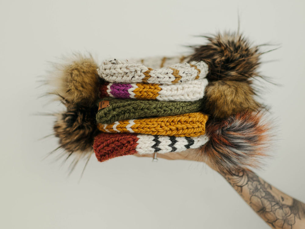 Stack of colorful behappe knitted hats with fur trim on a white background