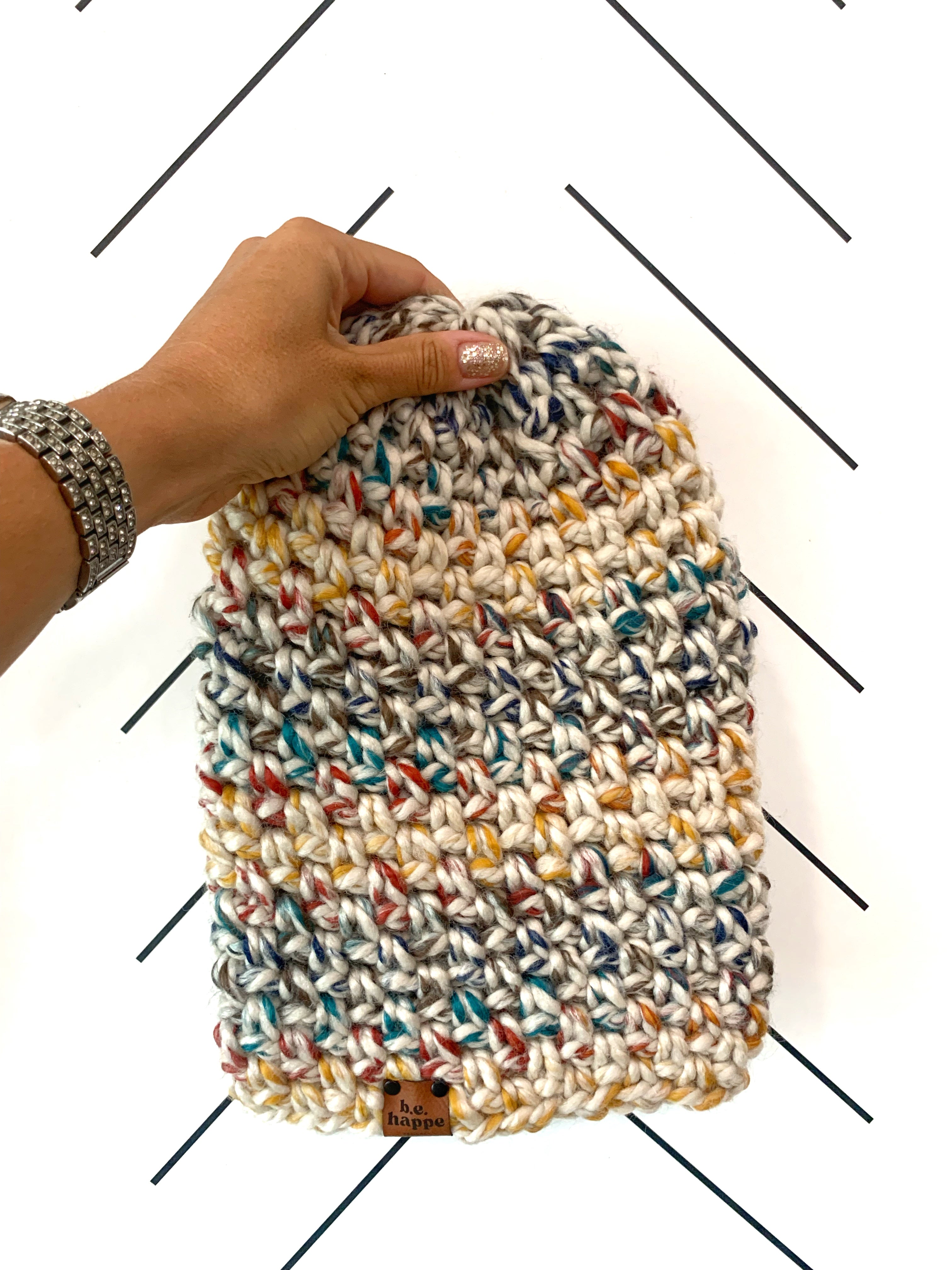 A multicolored, hand-crocheted slouchy beanie being held by a hand against a white background.