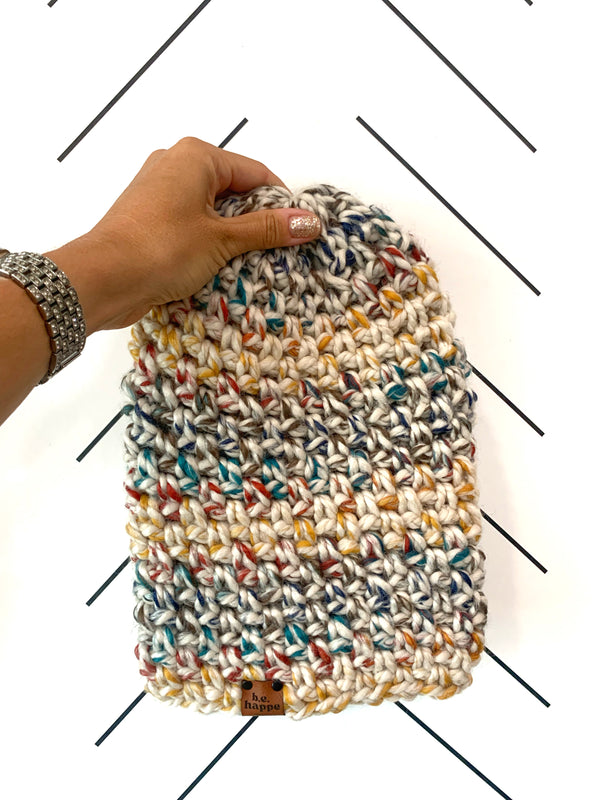 A multicolored, hand-crocheted slouchy beanie being held by a hand against a white background.