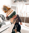 baby wearing behappe green and white striped faux fur pom beanie